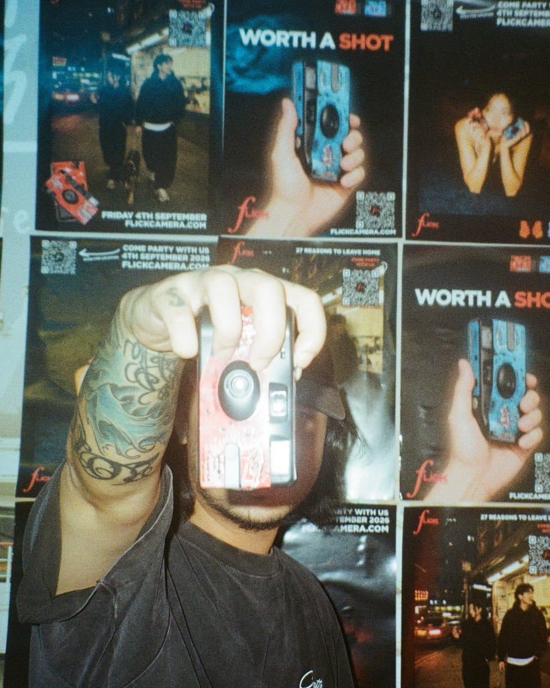 Guest holding a red Flick camera up to the lens, mirroring the campaign poster behind him